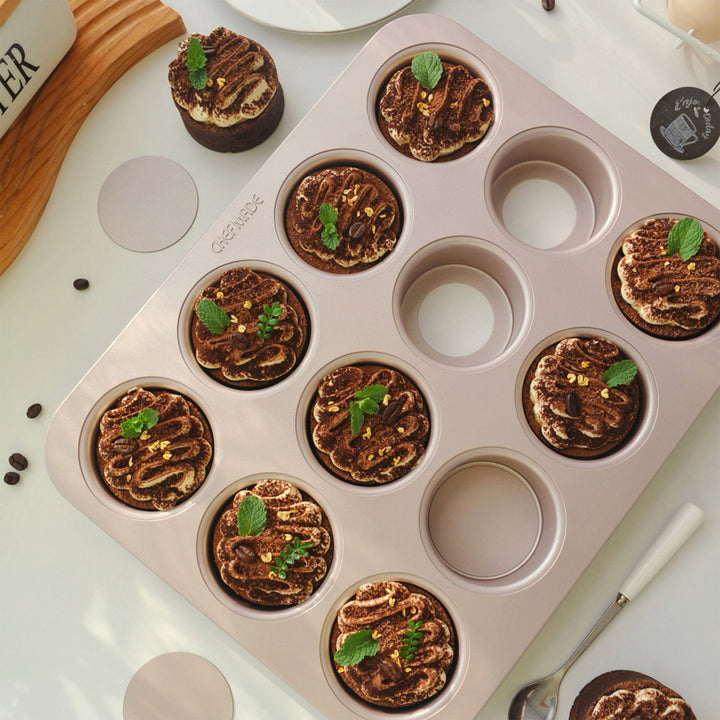 Muffin tin with chocolate muffins topped with mint leaves on a light surface.