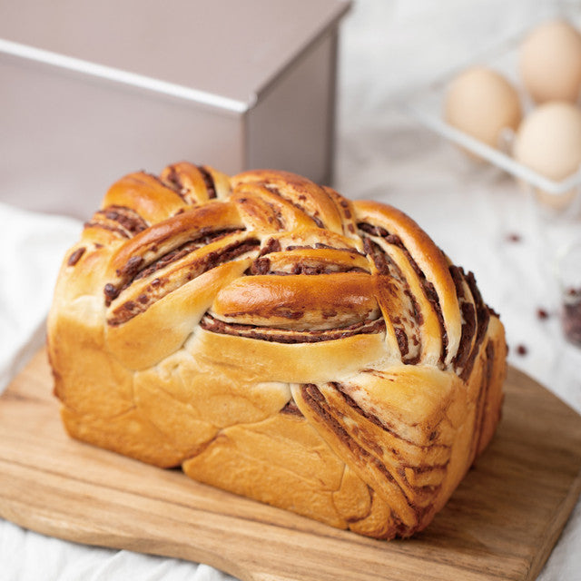 Braided bread loaf on a wooden cutting board with eggs in the background