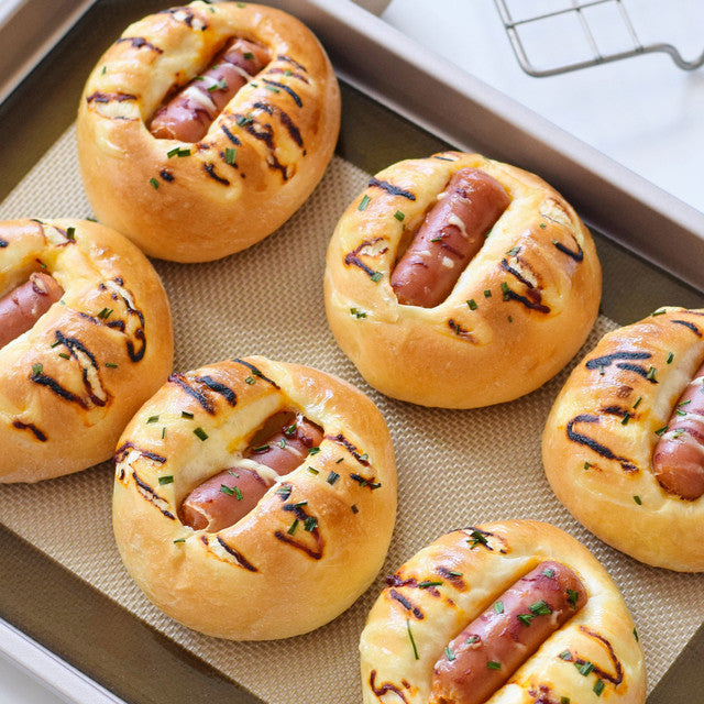 Hot dogs in bread buns on a baking tray with a laptop in the background