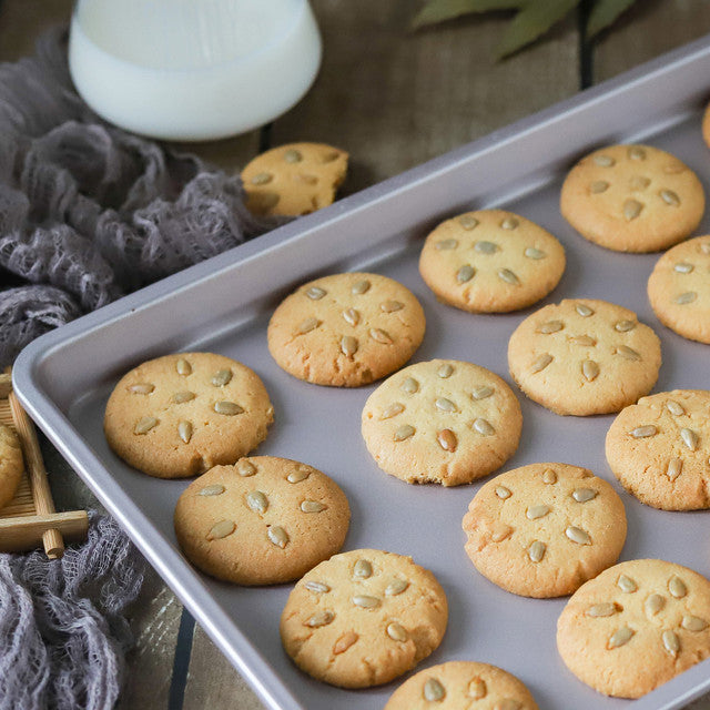Biscuits with seeds on a baking tray next to a glass of milk.
