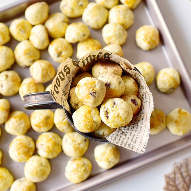 Small round baked goods in a scoop with newspaper, on a baking tray with more of the same items.