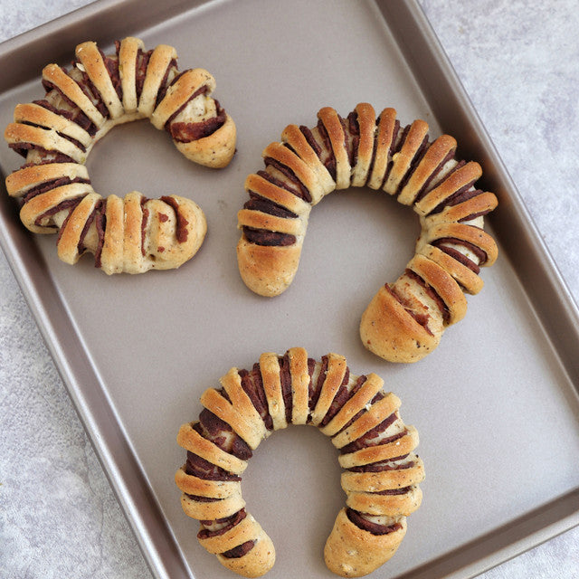 Three crescent roll wreaths with a filling on a baking tray.
