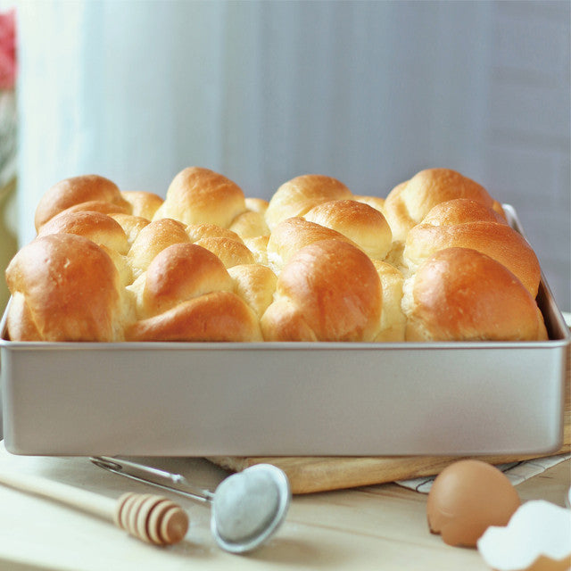 Baked rolls in a pan with a honey dipper and eggs on a wooden surface