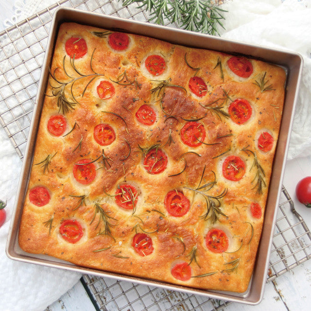Baked focaccia bread with tomatoes and rosemary on a baking tray.