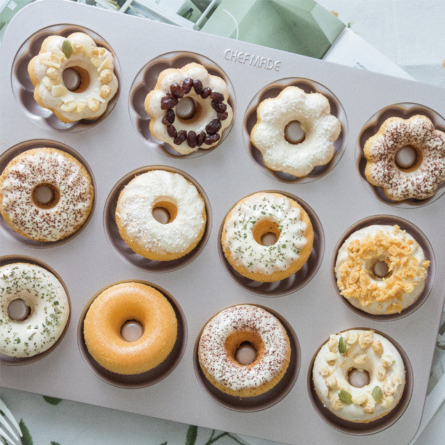 Donut-shaped baking mold with various donut toppings on a light background