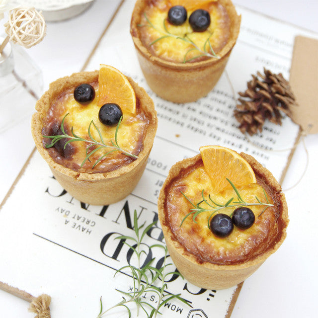Three small pies with orange slices and blueberries on a newspaper background