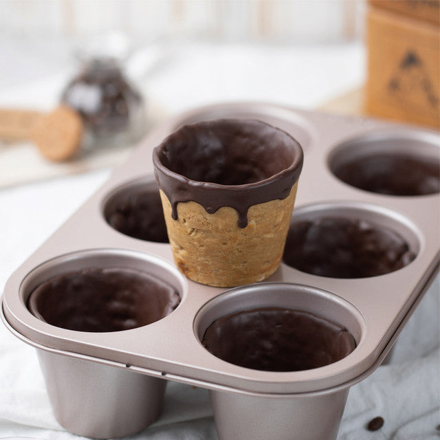 Metal muffin tin with chocolate cups and a cookie cup on a kitchen counter.