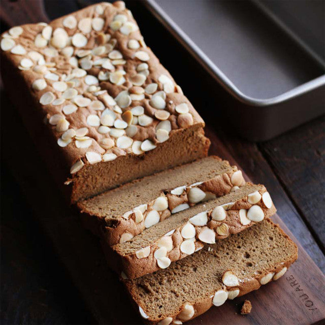 Loaf of bread with nuts on top, sliced, on a wooden cutting board.