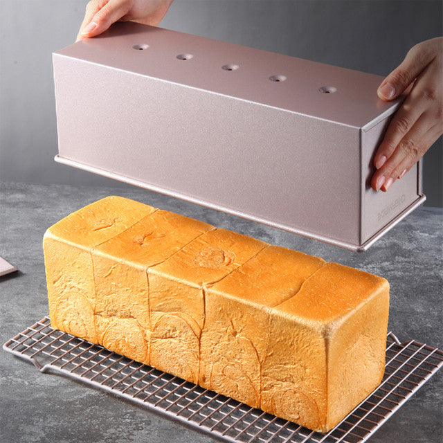 Baked loaf of bread with a metal loaf pan on a cooling rack