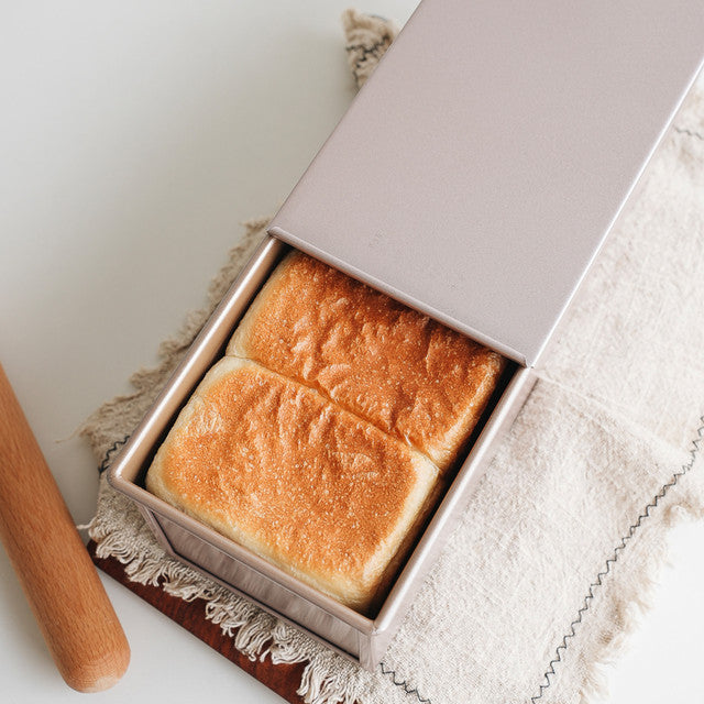 Loaves of bread in a box on a white surface with a rolling pin.