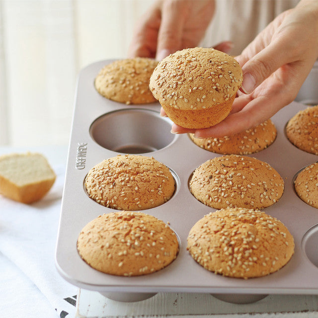 Muffin tray with baked muffins, one being held by a hand.