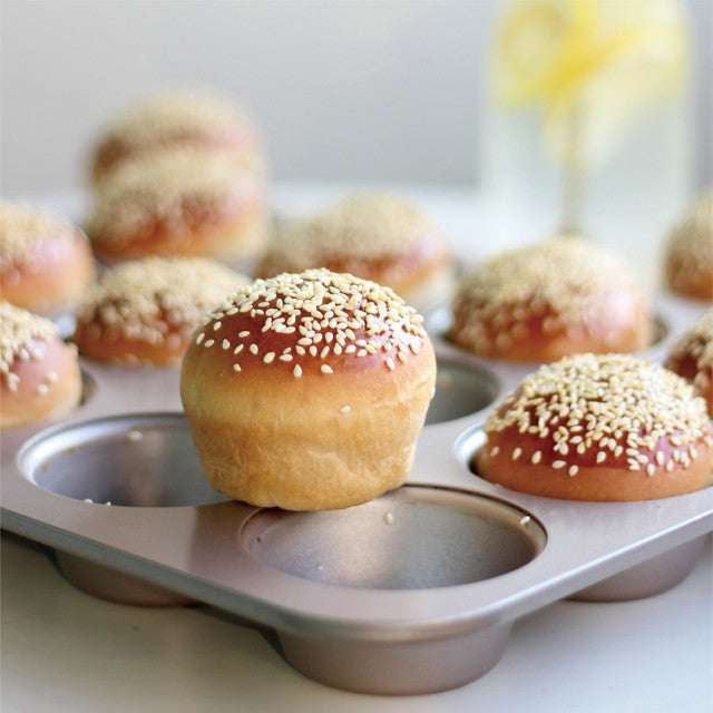 Baked goods with sesame seeds in a muffin tin on a light background