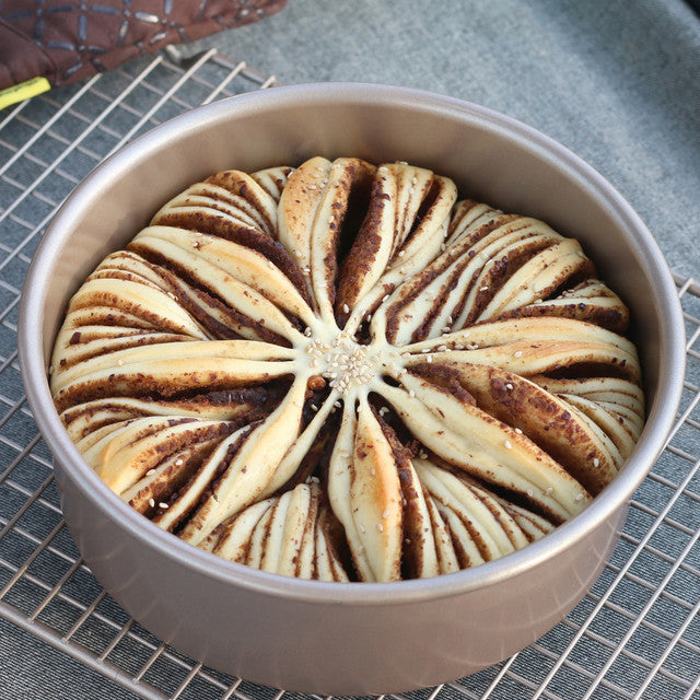 Baked pastry with a spiral pattern in a round baking dish on a cooling rack.