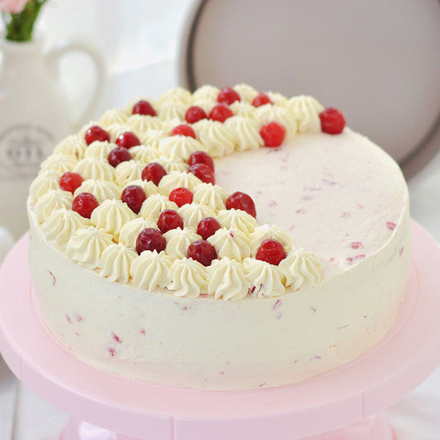 White cake with red berries on a pink stand