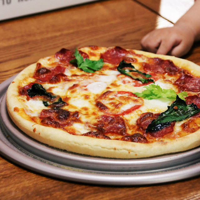 Personal-sized pizza with pepperoni and spinach on a wooden table