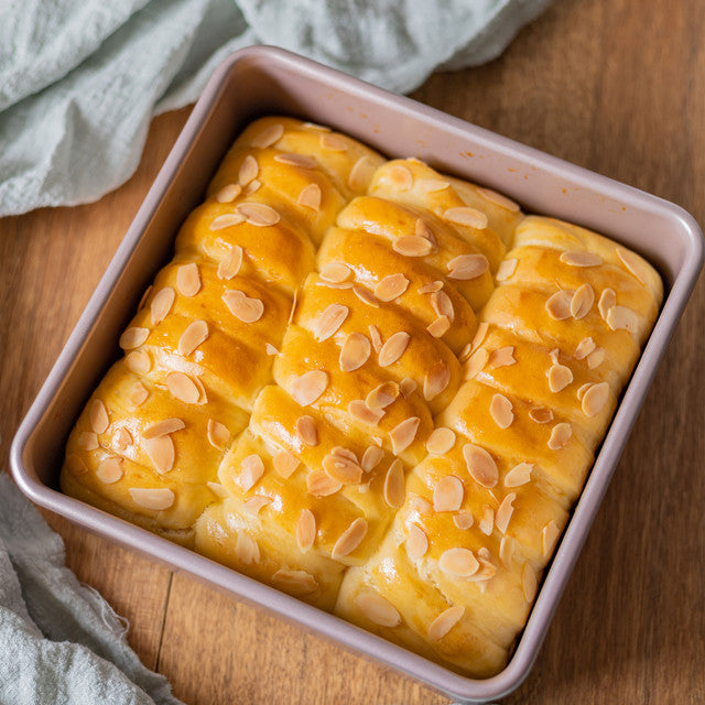 Baked good with a golden-brown crust in a pink baking dish on a wooden surface