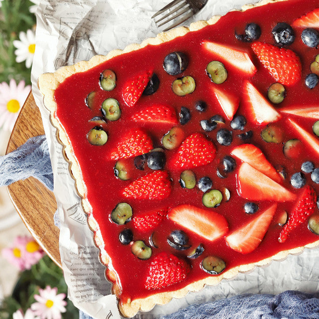 Fruit tart with strawberries, blueberries, and kiwis on a wooden board.