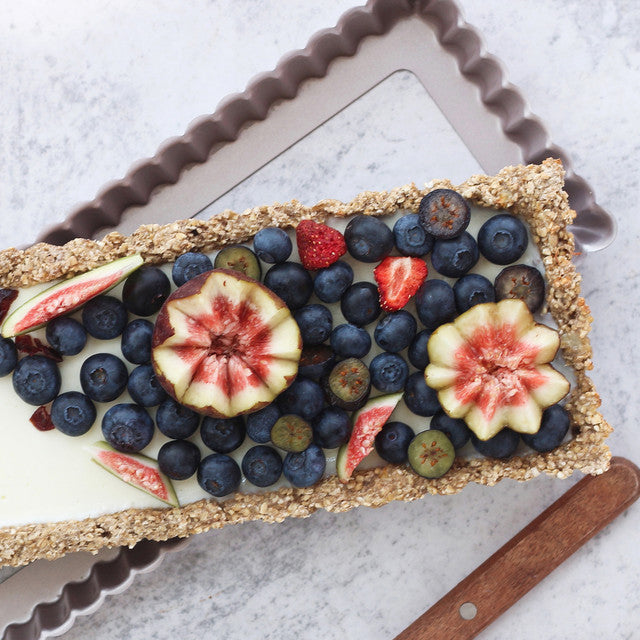 Fruit tart with blueberries, figs, and raspberries on a white surface