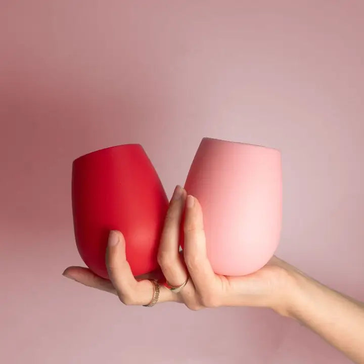Two silicone stemless wine glasses, one red and one light pink, held in a person&