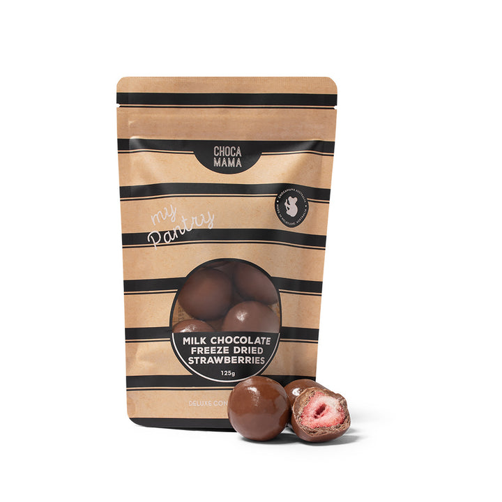 A stand-up pouch of Choca Mama Milk Chocolate Freeze Dried Strawberries, featuring a kraft paper design with black stripes and a clear window showing the chocolate spheres inside. Two chocolate strawberries are displayed in front of the package, one whole and one cut open to show the pink strawberry filling.