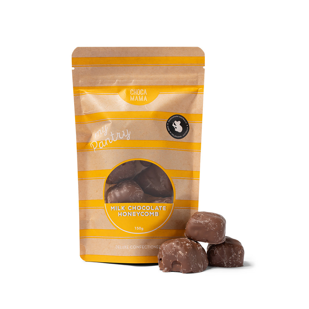 A stand-up pouch of milk chocolate honeycomb candies with three loose chocolate pieces placed in front on a clean white background. The packaging is tan and yellow striped with a circular window showing the dark chocolate pieces inside.