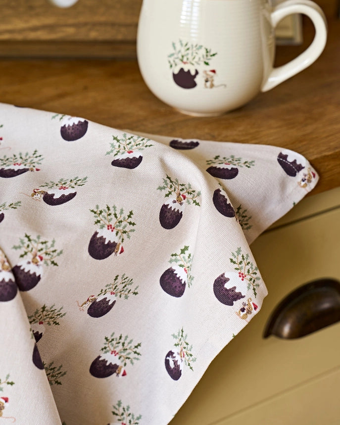 A fabric tea towel featuring a repeating pattern of Christmas puddings draped over a timber benchtop