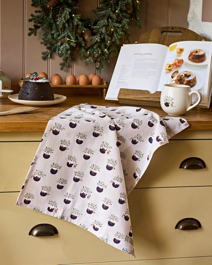 A fabric tea towel featuring a repeating pattern of Christmas puddings draped over a kitchen bench