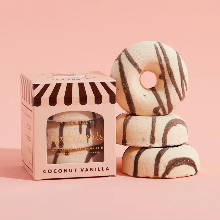Stack of coconut vanilla donut-shaped bath bombs with a striped box on a pink background