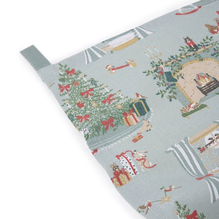 A rectangular fabric tea towel, featuring a festive Christmas pattern on a light blue-gray background. The pattern includes Christmas trees, stockings, fireplaces with Santa Claus, and small birds.