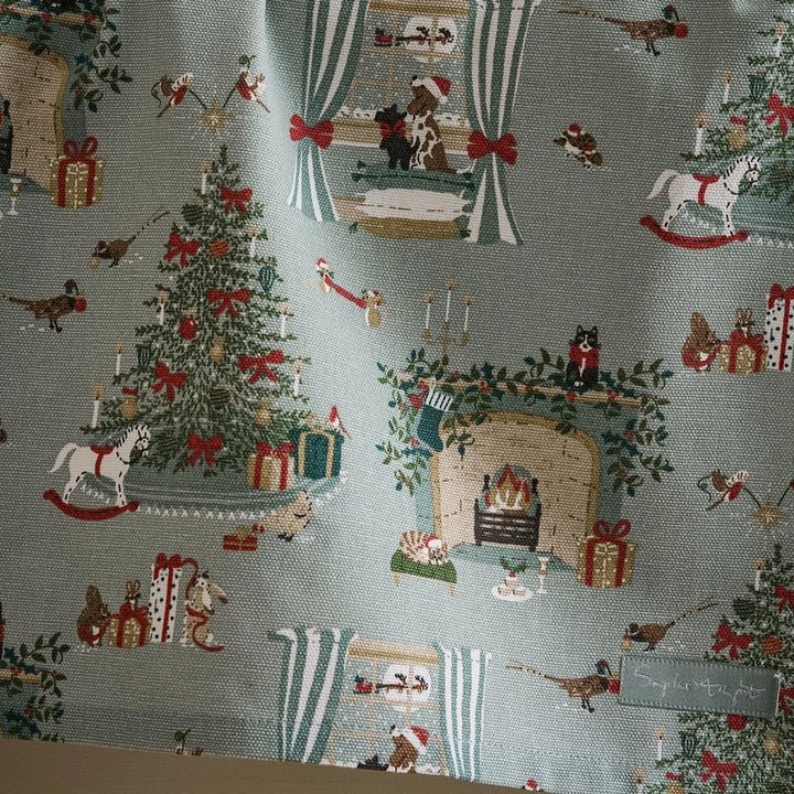 A fabric tea towel, featuring a festive Christmas pattern on a light blue-gray background. The pattern includes Christmas trees, stockings, fireplaces with Santa Claus, and small birds.
