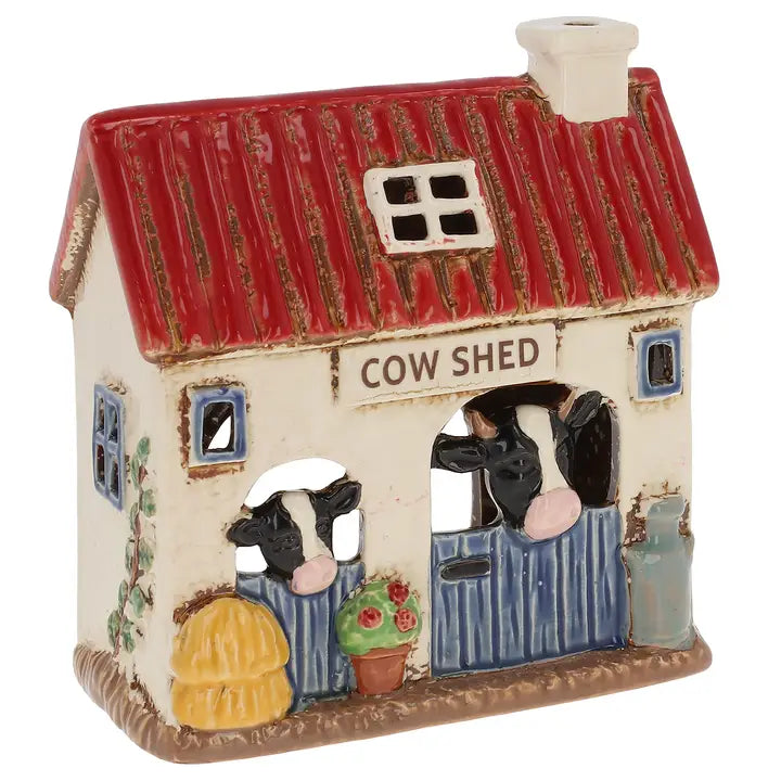 A ceramic tealight holder of a cow shed with cows on it on a white background