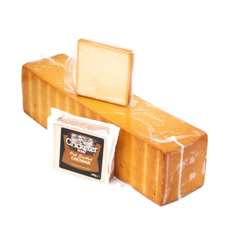 Two blocks of Cheddar cheese with a Cricketer Oak Aged Cheddar packaging on a white background
