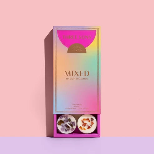 Three Suns Mixed Tea Light Collection in a rectangular iridescent box with a pink lid and two tea lights visible in the base, set against a pink background.