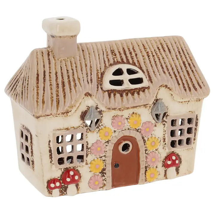 A ceramic house tealight holder with mushrooms and flowers on it on a white background