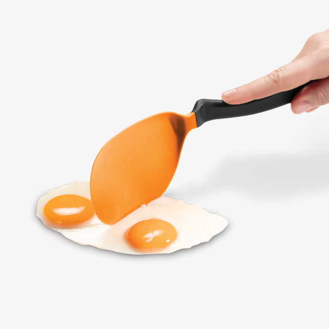 Orange spatula lifting a fried egg from a white surface