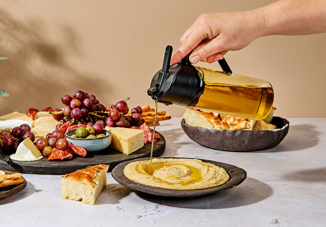 A hand drizzing olive oil from a lass bottle onto hummus