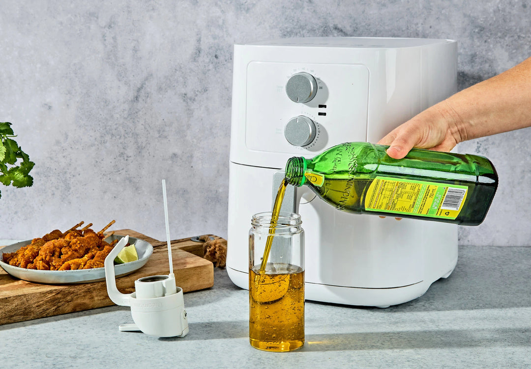 A hand decanting olive oil from a bottle into a olive oil mister
