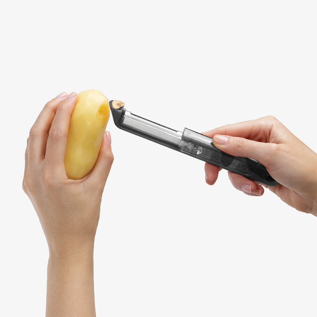 Person using a potato peeler on a potato against a white background