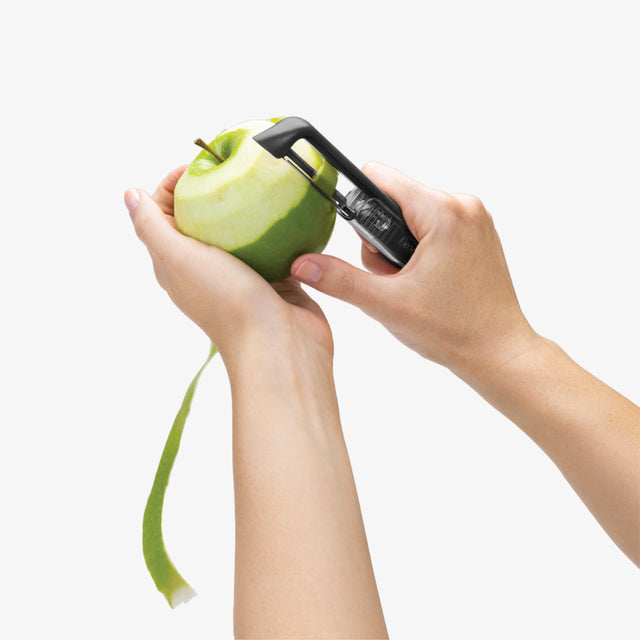 Person using a peeler on a green apple against a white background