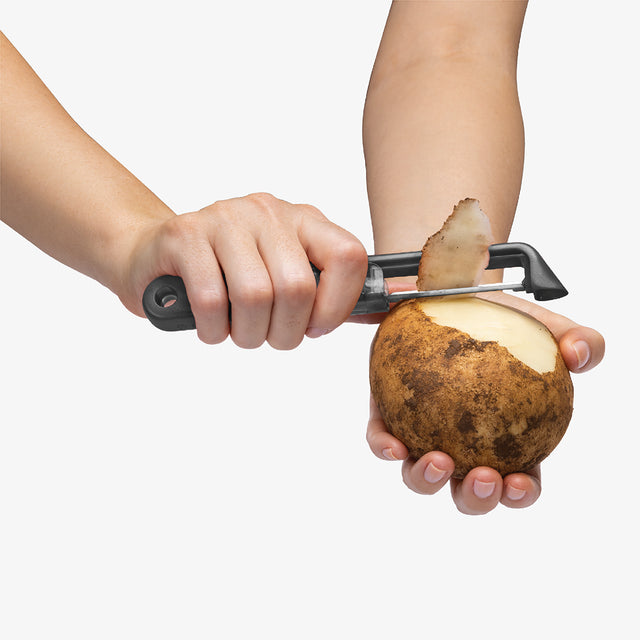 Person peeling a potato with a peeler on a white background