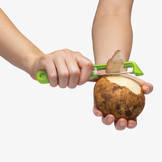 Person peeling a potato with a green peeler on a white background