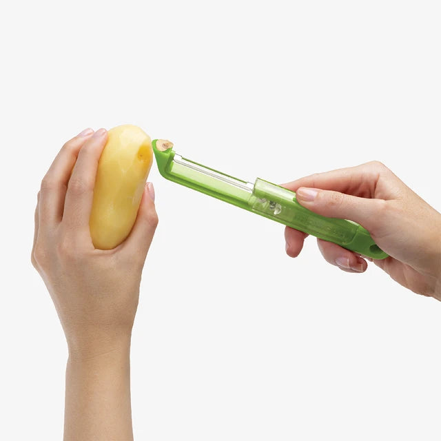 Person using a green vegetable peeler on a potato against a white background