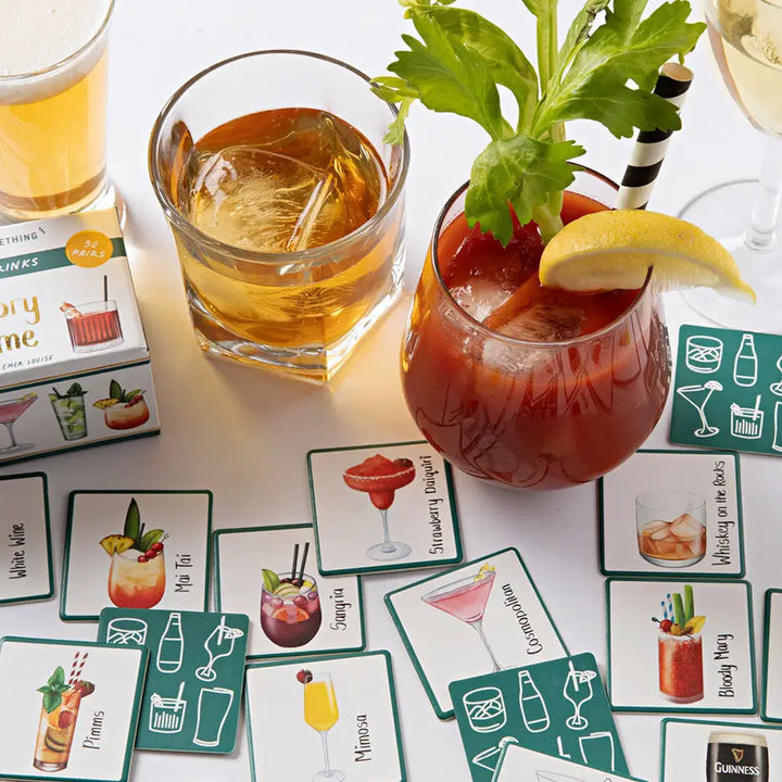 Mature cocktails with garnishes on a table with cocktail-themed cards.