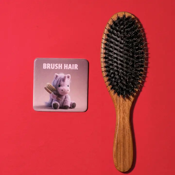 A wooden hairbrush with black bristles is shown next to a small square card that reads &