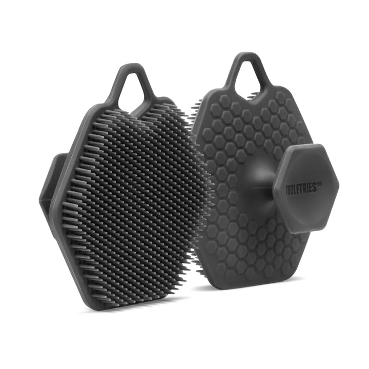Two grey silicone face scrubbers on a white background