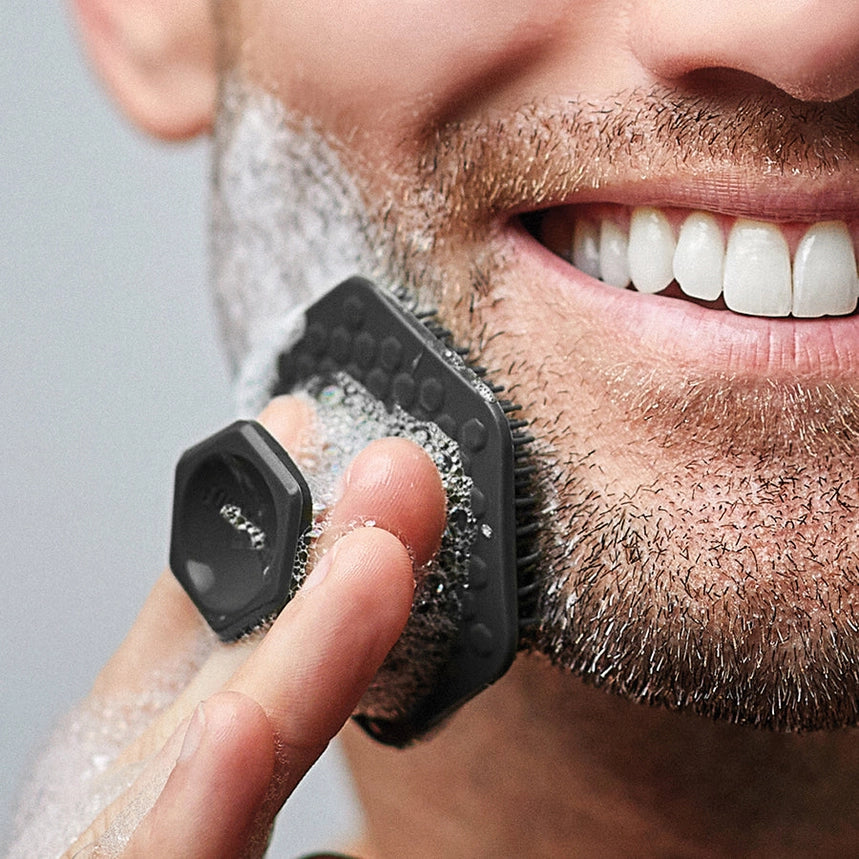 Man with a short beard washing face with foaming face wash on a black exfoliating scrubber