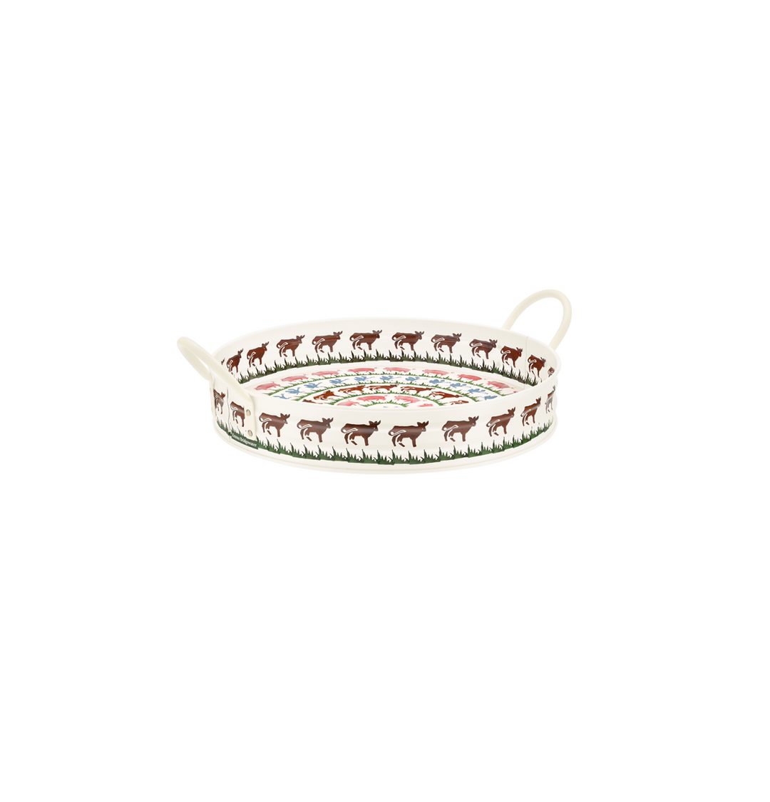 A round metal serving tray with two loop handles, decorated with a border of brown cow and green grass, pin pigs blue birds &amp; and a colorful floral pattern in the center, shown on a plain white background.