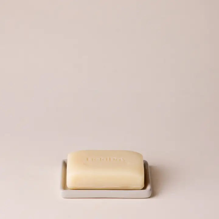 Bar of soap on a white soap dish with a plain background