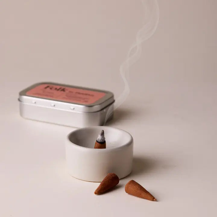 Incense cones and a small white dish with a lit incense cone on a light background