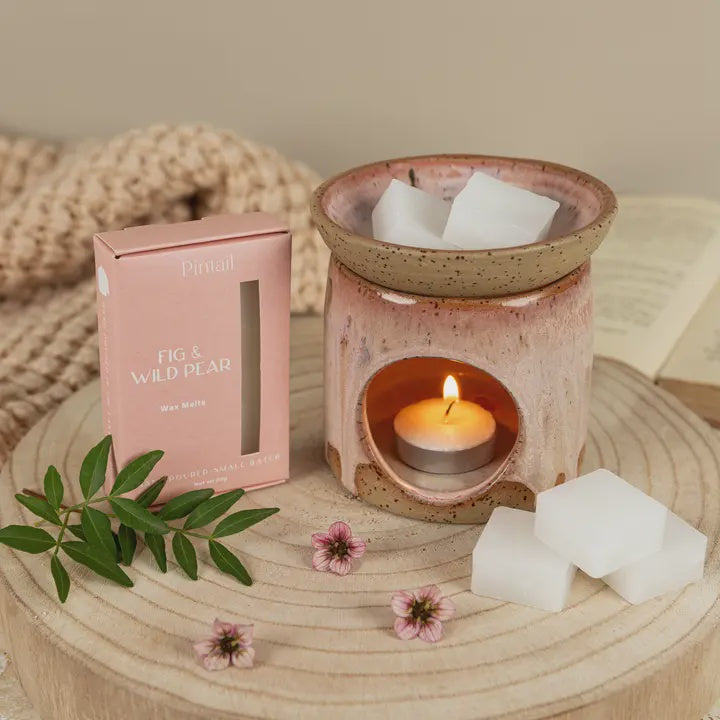Ceramic wax warmer with a lit candle, wax melts, and a pink box labeled &
